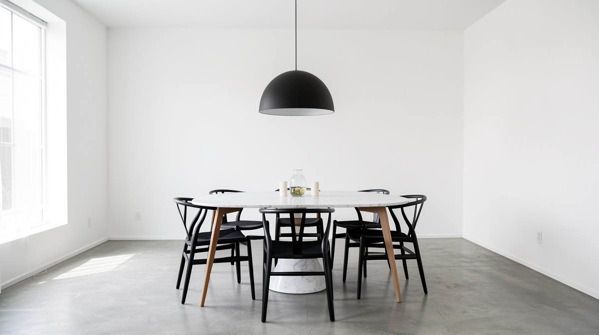 A dining room redesigned in modern style with a long marble table, slim cane-back chairs, a sculptural pendant light, and a single large abstract painting on the wall